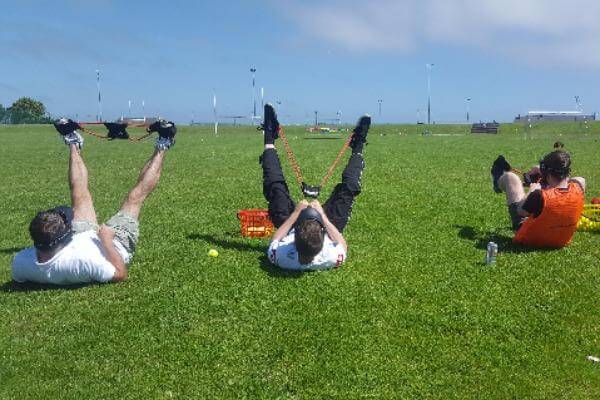 Players lying on the grass with catapult attached to feet.